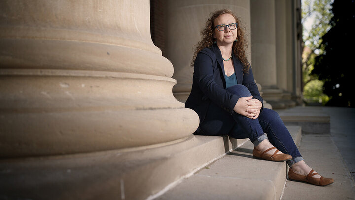Katrina Jagodinsky sitting on stone steps, leaning against a large column, wearing casual attire.